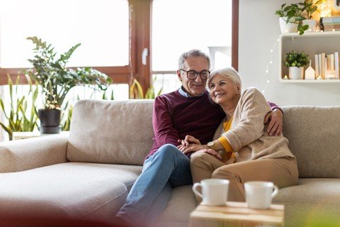 Retired couple sat at home on a sofa smiling